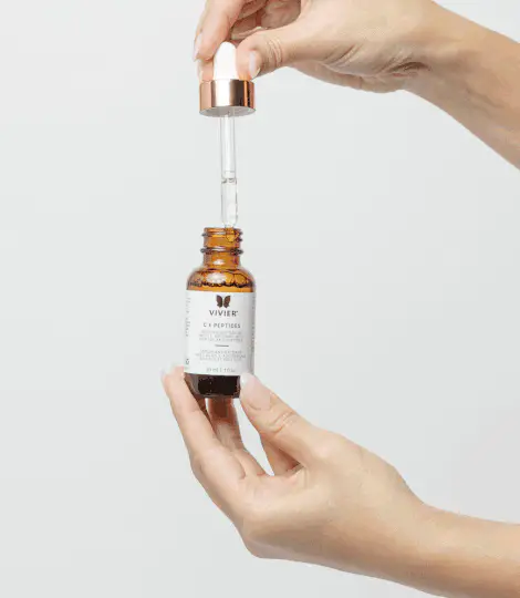Hands holding a Vivier C E PEPTIDES bottle with its dropper raised