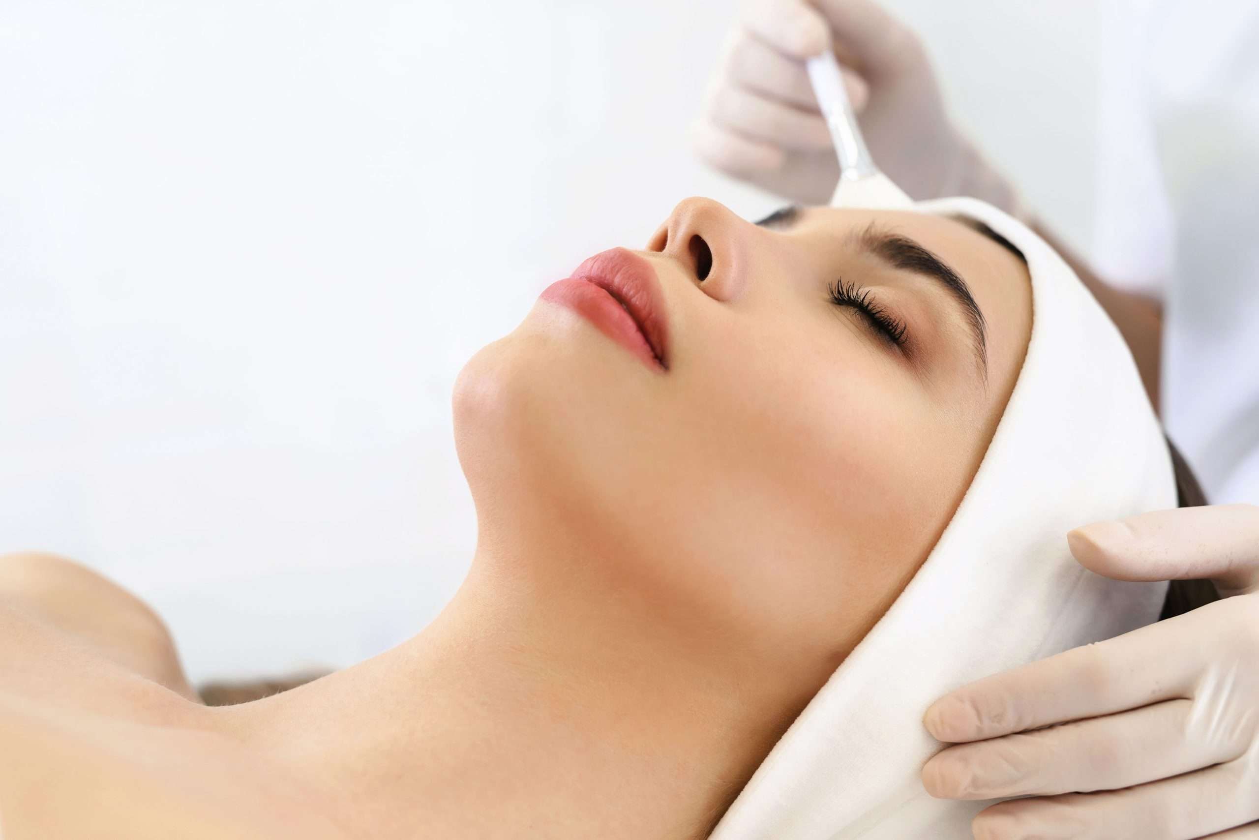 Woman reclining with eyes closed while a facial brush is used on her forehead