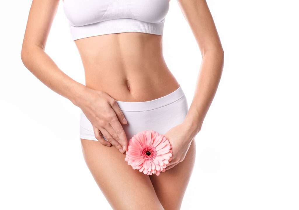Woman holding a pink flower in front of her lower abdomen